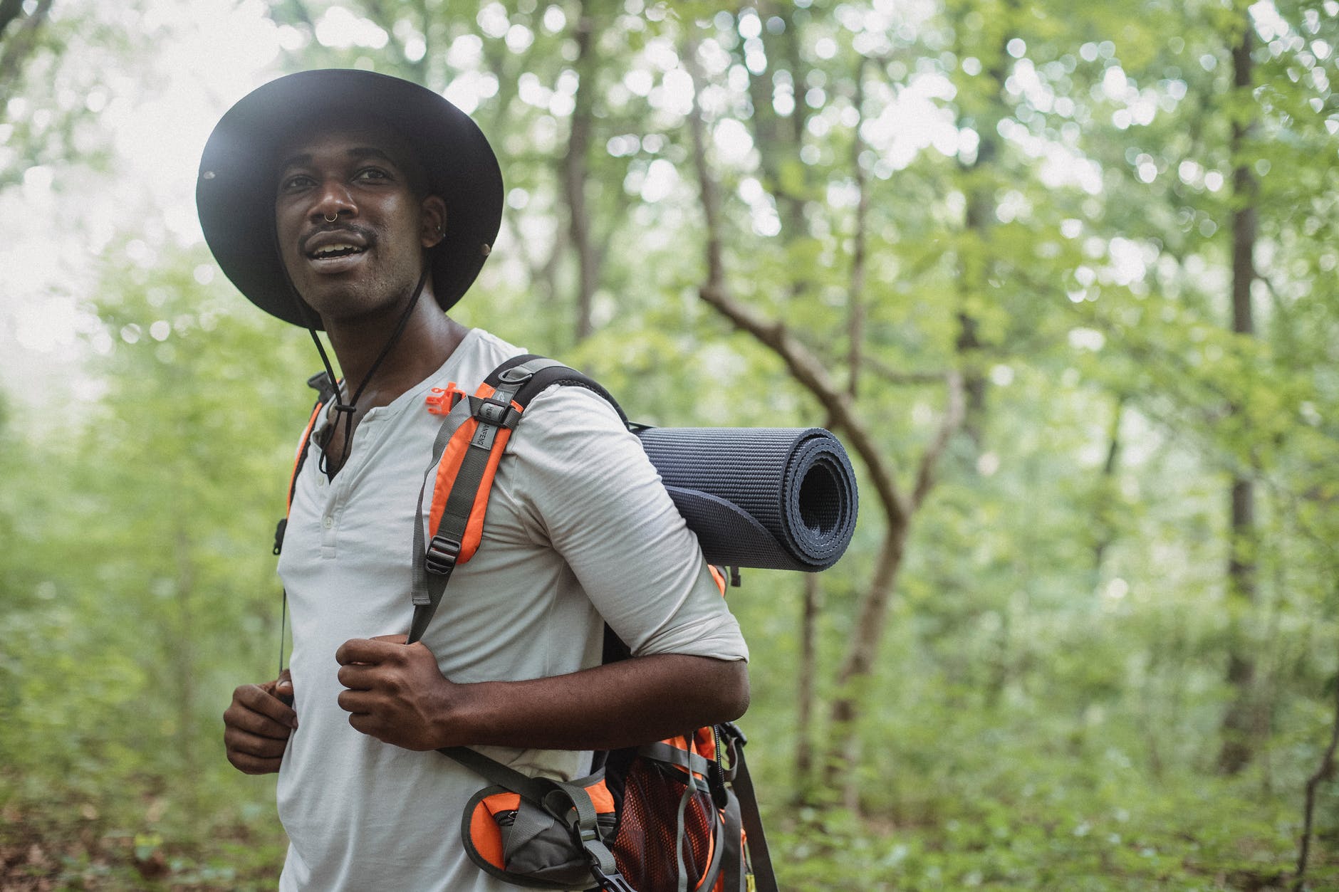positive black man standing with trekking backpack in forest